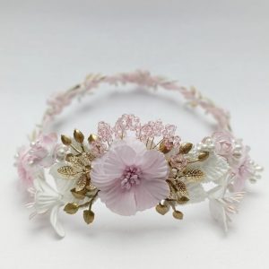 Corona de comunión artesanal en tonos rosa claro y blanco, con flores y detalles dorados.